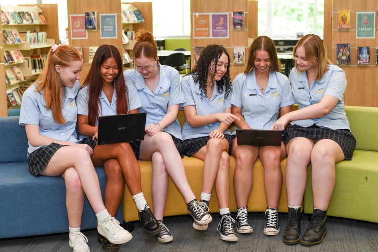 Six senior female students sitting on a lounge in the library working on laptops.